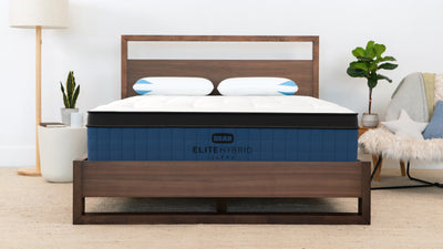 Mattress with 'ELITE ULTRA HYBRID' branding on a wooden bed frame in a bedroom setting.